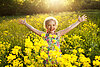 Fröhliches Kind in Blumenwiese mit gelben Blüten.