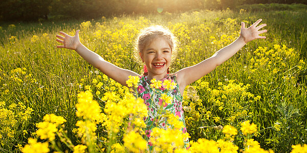 Fröhliches Kind in Blumenwiese mit gelben Blüten.