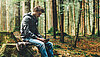 Ein junger Mann sitzt im Wald und benutzt ein digitales Tablet
