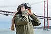 Frau trägt eine Brille für virtuelle Realität. Im Hintergrund ist eine rote Hängebrücke zu sehen.