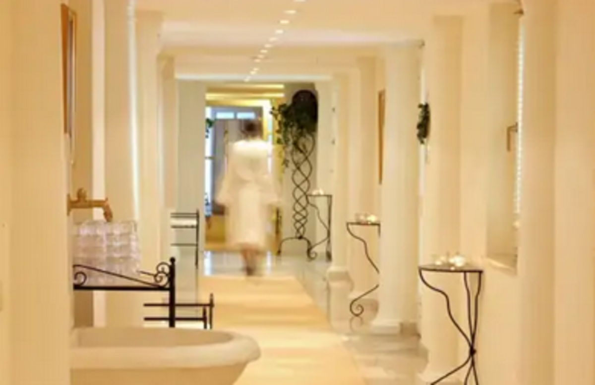 Langer Gang mit beigen Säulen und kleinen Tischen, Mann im Bademantel läuft im Hintergrund