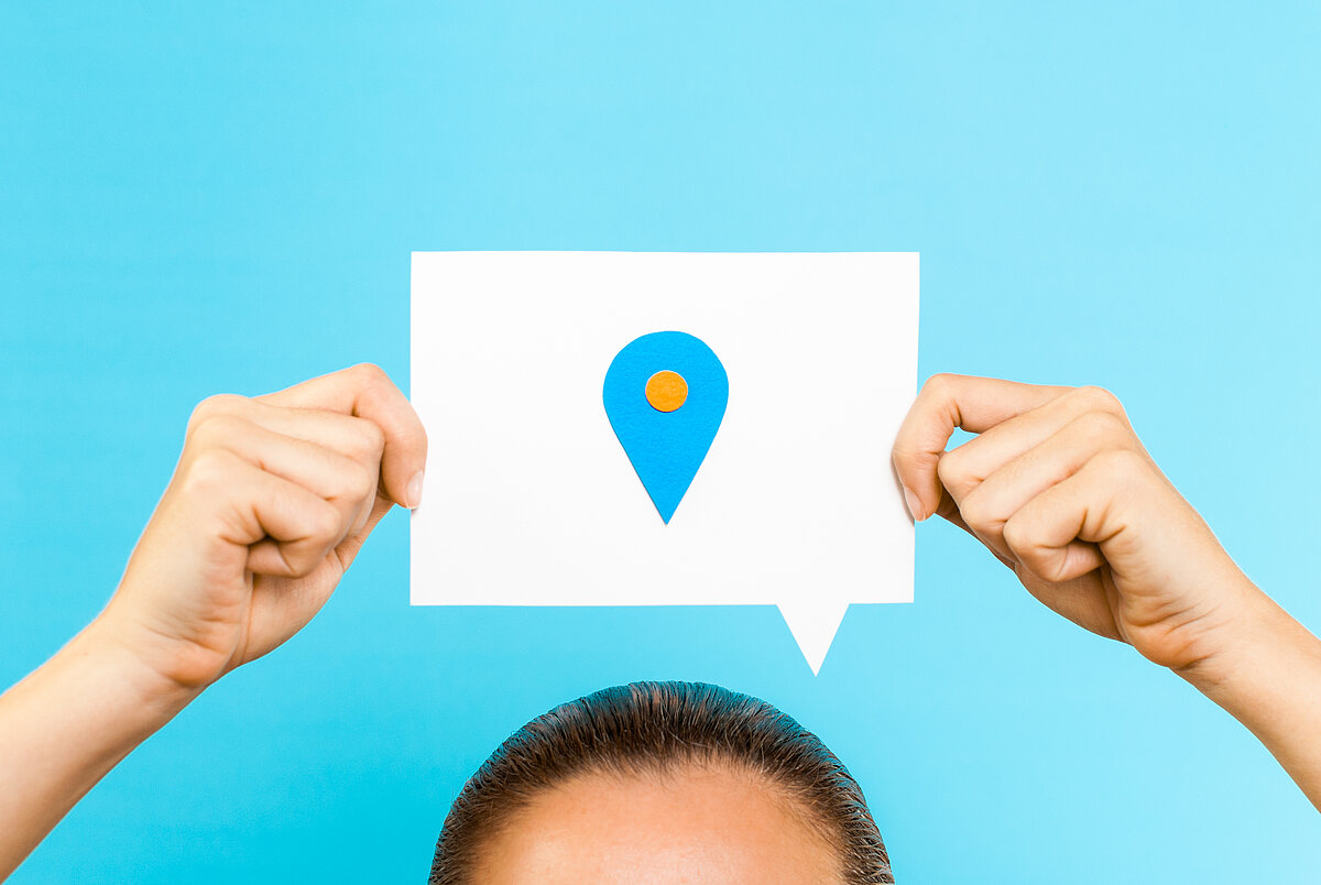 Frau hält ein Blatt mit Ortskennzeichnung über dem Kopf