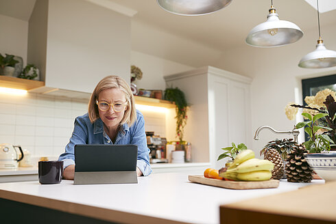 Frau sitzt in der Küche und arbeitet an ihrem Laptop